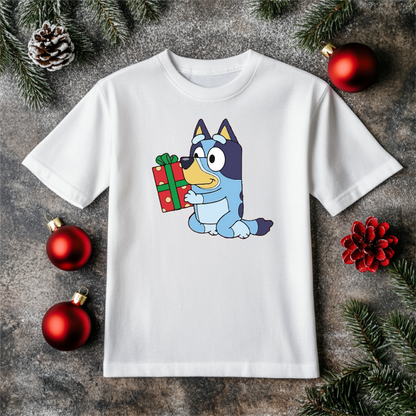 "Bluey's Christmas Cheer" youth holiday shirt featuring an adorable Bluey-inspired pup holding a Christmas gift, styled on a white T-shirt with festive decorations.