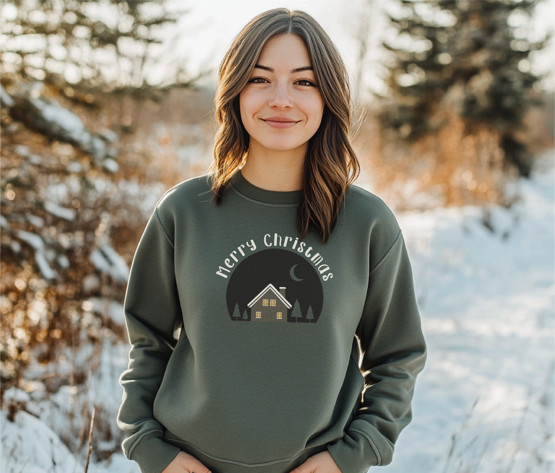 Cozy Christmas shirt featuring a winter cabin under a crescent moon, surrounded by evergreens, modeled outdoors in a snowy setting.