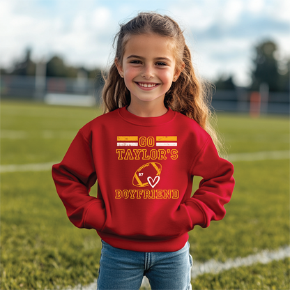 Child wearing a red 'Go Taylor's Boyfriend' sweatshirt with football and heart graphic, standing on a football field.