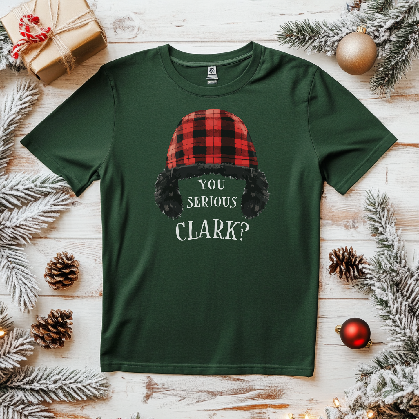 "You Serious Clark?" holiday shirt featuring a red and black plaid winter hat and humorous quote, styled on a green T-shirt surrounded by festive decorations.